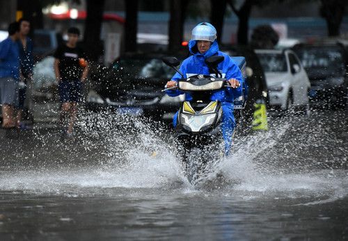 7月16日，一名快餐配送员从北京西城区一段积水的路面骑过。新华社记者