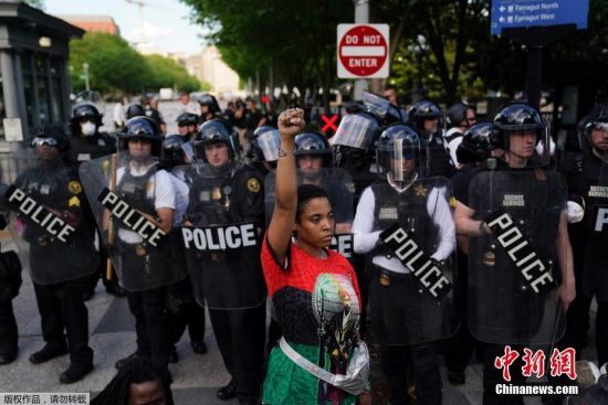 当地时间5月30日，一名抗议者者在警察组成的人链前高举拳头示威。