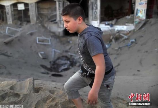 当地时间5月12日，巴以冲突期间，一名巴勒斯坦男孩儿在满是尘土的街头行走。
